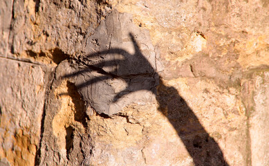 The strange shadow of one hand on an old stone wall. Black shadow, female hand. Background, texture, cropped image, horizontal, abstraction. The concept of fear.