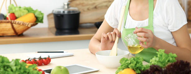 Beautiful Hispanic woman cooking in kitchen while using tablet computer and wooden spoon. Housewife found new recipe for dinner or breakfast. Healthy meal and householding concepts