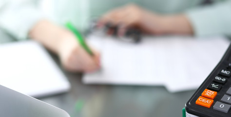 Bookkeeper or financial inspector  making report, calculating or checking balance. Binders with papers and calculator closeup. Audit and tax service concept. Green colored image background 