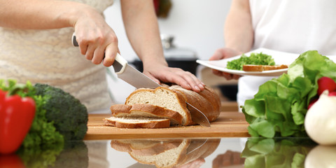 Closeup of human hands cooking in kitchen. Mother and daughter or two female friends cutting bread for dinner. Friendship, family and lifestyle concepts
