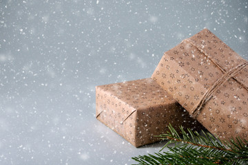 Christmas gifts wrapped in craft paper with twine and green spruce branches in snow on grey background with copy space