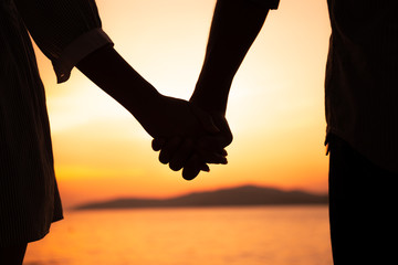 Couple hold hands in summer time on sunset at beach