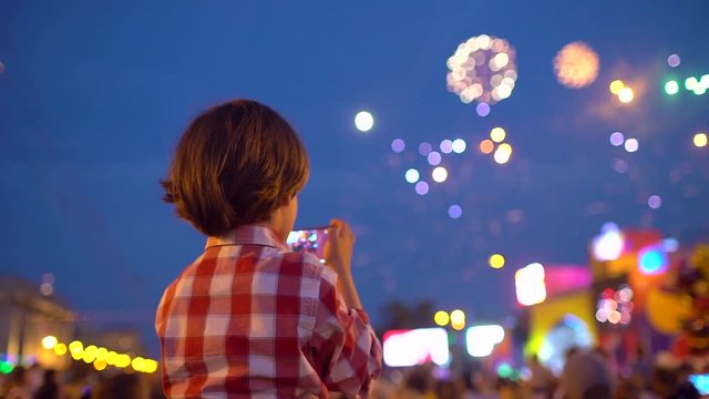 Little boy child filming pictures of beautiful fireworks in night sky display of mobile phone. Hands of baby taking video photo of firework on smartphone. Celebration happy holiday people family
