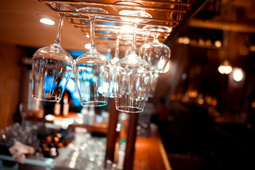 Fototapeta na wymiar Glasses of wine. Glasses hanging above the bar in the restaurant. Empty glasses for wine. Wine and martini glasses in shelf above a bar rack in restaurant. blue lights, blue background, night life