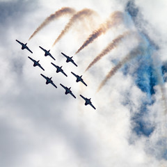 Silhouette of Airshow Fighter Jet airplanes in formation through big white clouds and a bright blue sky.  