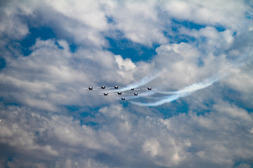 Silhouette of Airshow Fighter Jet airplanes in formation through big white clouds and a bright blue sky.  