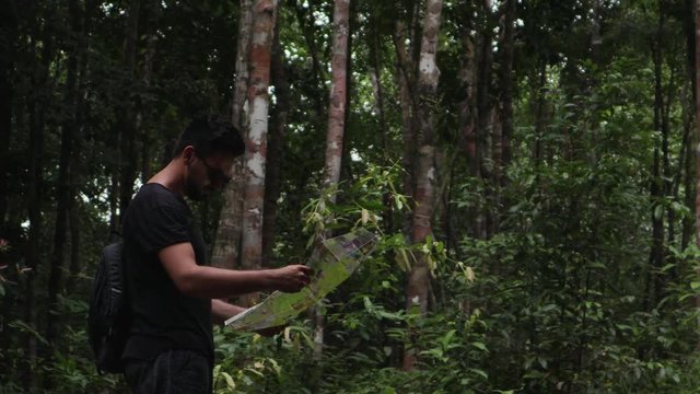 Cinematic footage. Young handsome man looking for the right way at the tropical jungles using a map.