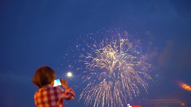Little boy child filming pictures of beautiful fireworks in night sky display of mobile phone. Hands of baby taking video photo of firework on smartphone. Celebration happy holiday people family