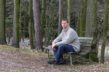 Fototapeta premium Portrait of young man sit on old bench in sweater from front