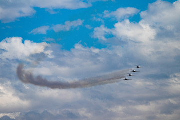 Formation of jet airplanes flying through the blue sky and clouds with smoke trails. 