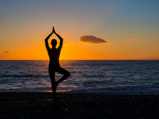 Silhouette of a young woman doing yoga on the beach at sunset