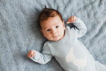 Newborn pretty baby boy in blue sleepwear lying on grey sheet, top view