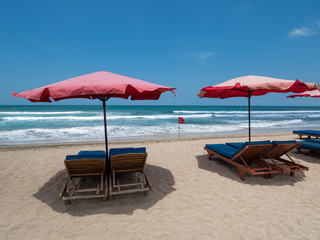 Red sun umbrellas stay on white sand beach with blue sea and blue sky on background. Concept for rest, relaxation, holidays, spa, resort. Bali, Indonesia, october 2018
