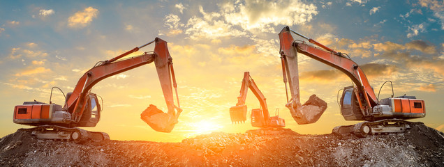 Three excavators work on construction site at sunset,panoramic view - obrazy, fototapety, plakaty