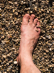 View of the foot of a man who is covered with stones and sand on the beach.