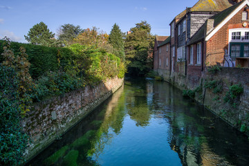 Fototapeta premium Landscape view of river Great Stour passing near houses. Green trees in the background. Canterbury, United Kingdom.