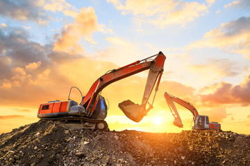 Two excavators work on construction site at sunset