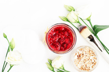 Top view white table background skincare spa ingredients for natural skin exfoliation with fresh ripe raspberry and oatmeals in jar, rose flowers & brush