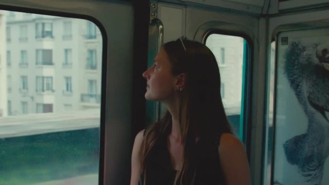 Young confident woman looks out through the train window at the European city passing by