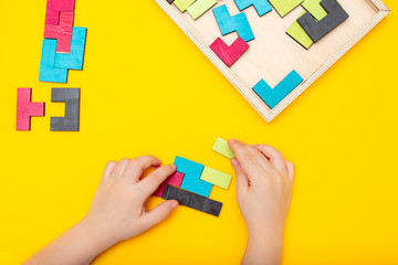Wooden puzzle and kids hands on yellow background. Flat lay