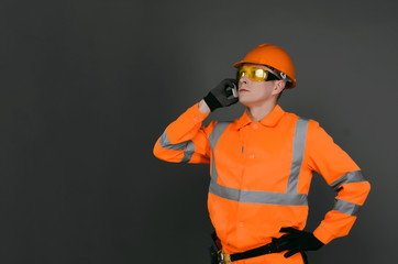 Builder worker in a hardhat is talking on a mobile phone and is looking up isolated on gray background with copy space.