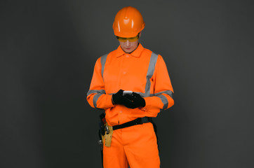 Builder worker in a hardhat is typing a sms message on a mobile phone in his hands isolated on gray background.