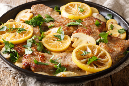 Tasty Italian fillet of veal scaloppini with mushrooms and lemons in sauce close-up in a frying pan. horizontal