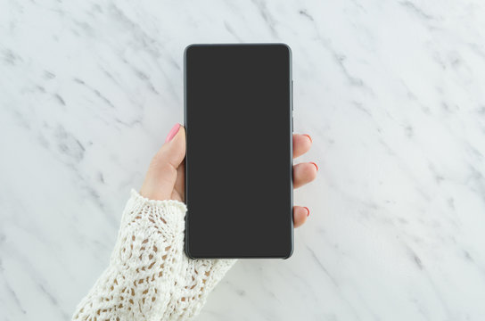 Woman hand holding black phone on marble background. Smartphone mockup