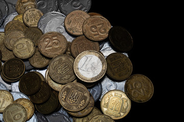 Ukrainian coins with one euro coin isolated on black background. Close-up view. Coins are located at the left side of frame. A conceptual image.