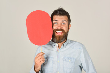 Smiling bearded man hold paper nameplate. Feeling&emotions. Facial expression. Fashion, beauty, hairdressing, barber salon. Laughing man with beard&mustache. Red blank paper. Man with empty name card.