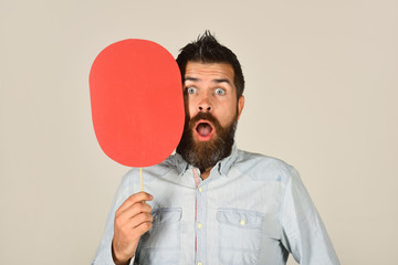 Surprised bearded man hold paper nameplate. Feeling&emotions. Facial expression. Fashion, beauty, hairdressing, barber salon. Amazed man with beard&mustache. Red blank paper. Man with empty name card.