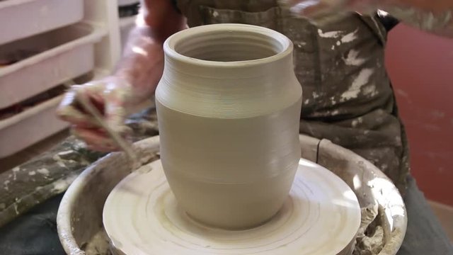 Potter creating a ceramics clay vase. Man sculptor in the workshop makes a jug out of earthenware closeup. Twisted potter's wheel. Hands detail. Small business concept.