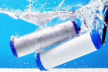 New carbon filter cartridge for house water filtration system isolated on blue background. Splash....