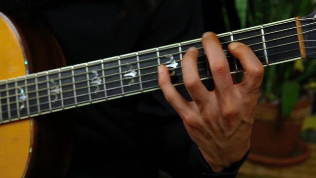 Man is playing acoustic guitar at home. Panning left scene on a professional guitarist practicing sweep picking and classical techniques at home