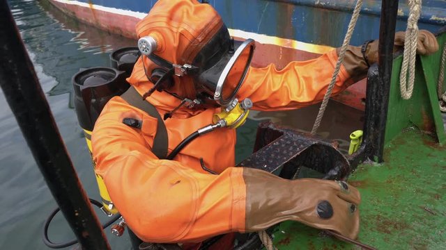 Professional diver in an orange diving suit stands on ship ladder before diving into ocean to carry out repair diving work of ship under water. Kamchatka Peninsula,  Pacific Ocean,  Russian Far East.