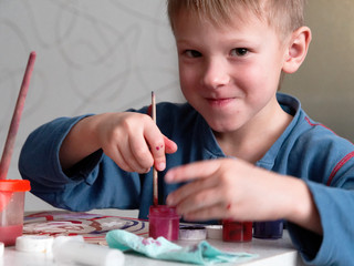 child boy enthusiastically paints with watercolors on paper.