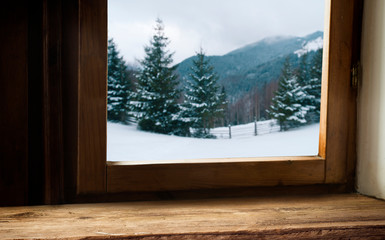Wooden table with space for your product. Curtain in the window. Open window with snowflakes. Landscape of winter forest. Morning sunshine.