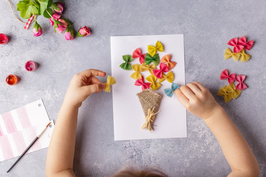 Paper crafts for mother day, 8 march or birthday. Small child doing a bouquet of flowers out of colored paper and colored pasta for mom. Simple gift idea. view top, copy space
