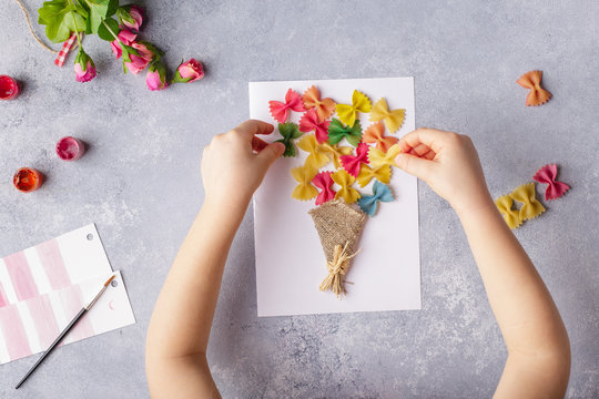 Paper Crafts For Mother Day, 8 March Or Birthday. Small Child Doing A Bouquet Of Flowers Out Of Colored Paper And Colored Pasta For Mom. Simple Gift Idea. View Top, Copy Space