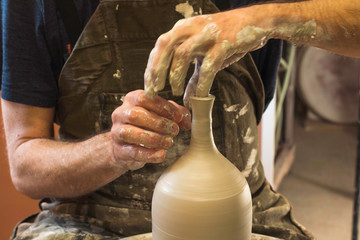 Potter creating a ceramics clay vase. Man sculptor in the workshop makes a jug out of earthenware closeup. Twisted potter's wheel. Hands detail. Small business concept.