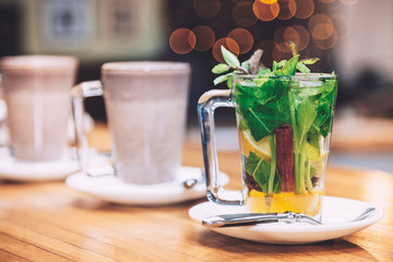 Cup of tea with mint, cinnamon and lemon of white plate. Nice red bokeh above the cup.