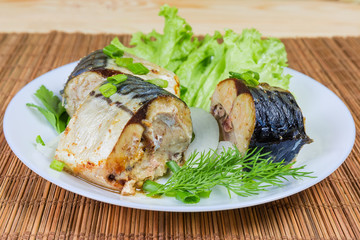 Sliced baked Atlantic mackerel with greens on dish close-up