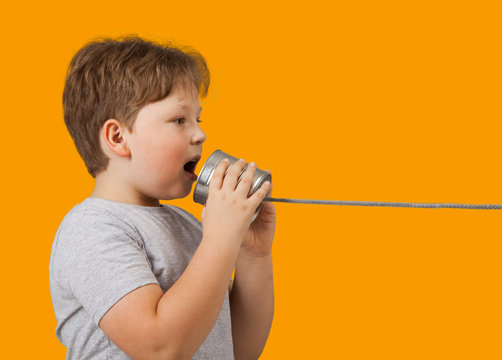 Boy Playing with Tin Can Phone. Isolated on Orange Background.