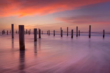 Gardinen Wooden poles on the beach at sunset © sara_winter