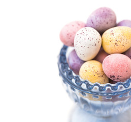 Chocolate candy Easter eggs in pastel colors in blue crystal cup, closeup, white background, styled image