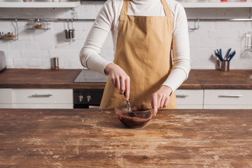 cropped shot of woman in apron preparing dough for gourmet homemade cake in kitchen