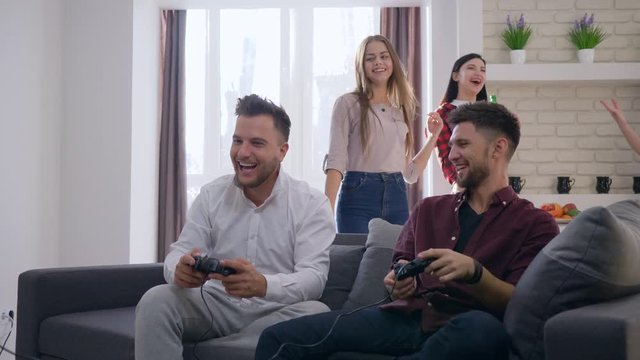 cheerful company of friends playing video games have fun and drink beer at the weekend in modern apartment