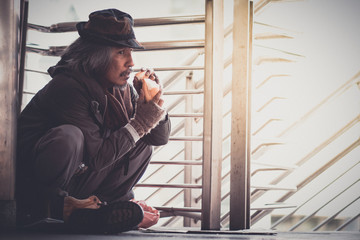Fototapeta premium Male Beggar, Homeless man on the corner of the walkway street in the city eating bread form kindness people give him.