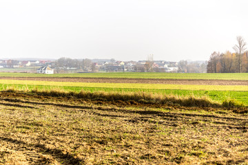 Fototapeta na wymiar Late autumn.Green meadows and plowed fields in the foreground.Lonely brick house in the background.Site about agroindustry, farming, weather, seasons.