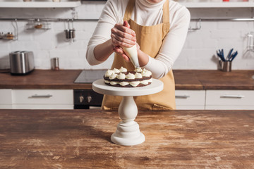 cropped shot of woman in apron decorating delicious sweet cake with cream